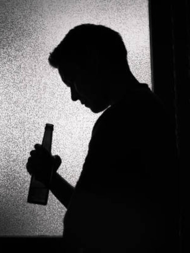 Unrecognizable sad man drinking a beer alone in a dark room.
